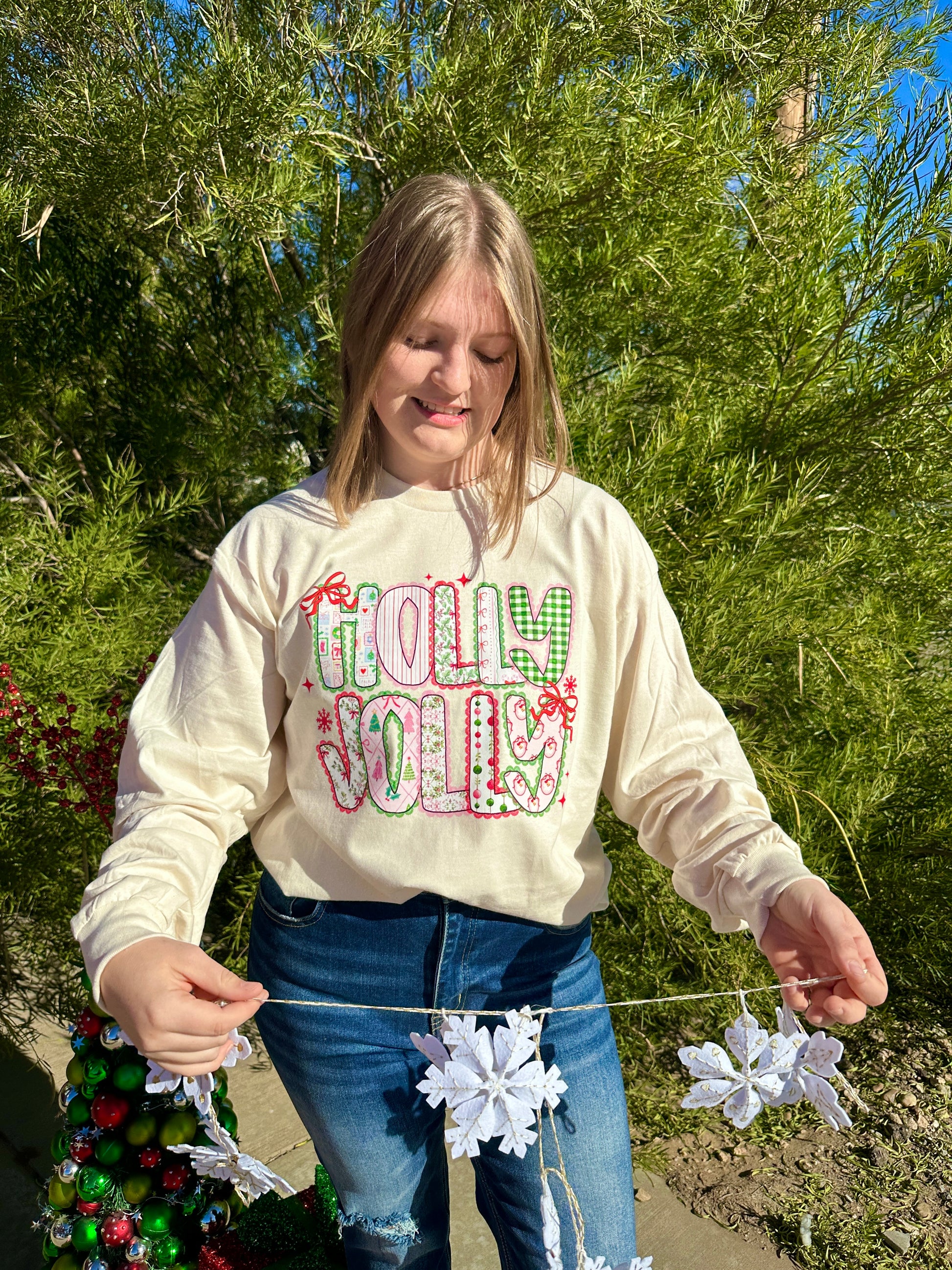 Person wearing a 'Holly Jolly' Long Sleeve T-Shirt outdoors with trees in the background