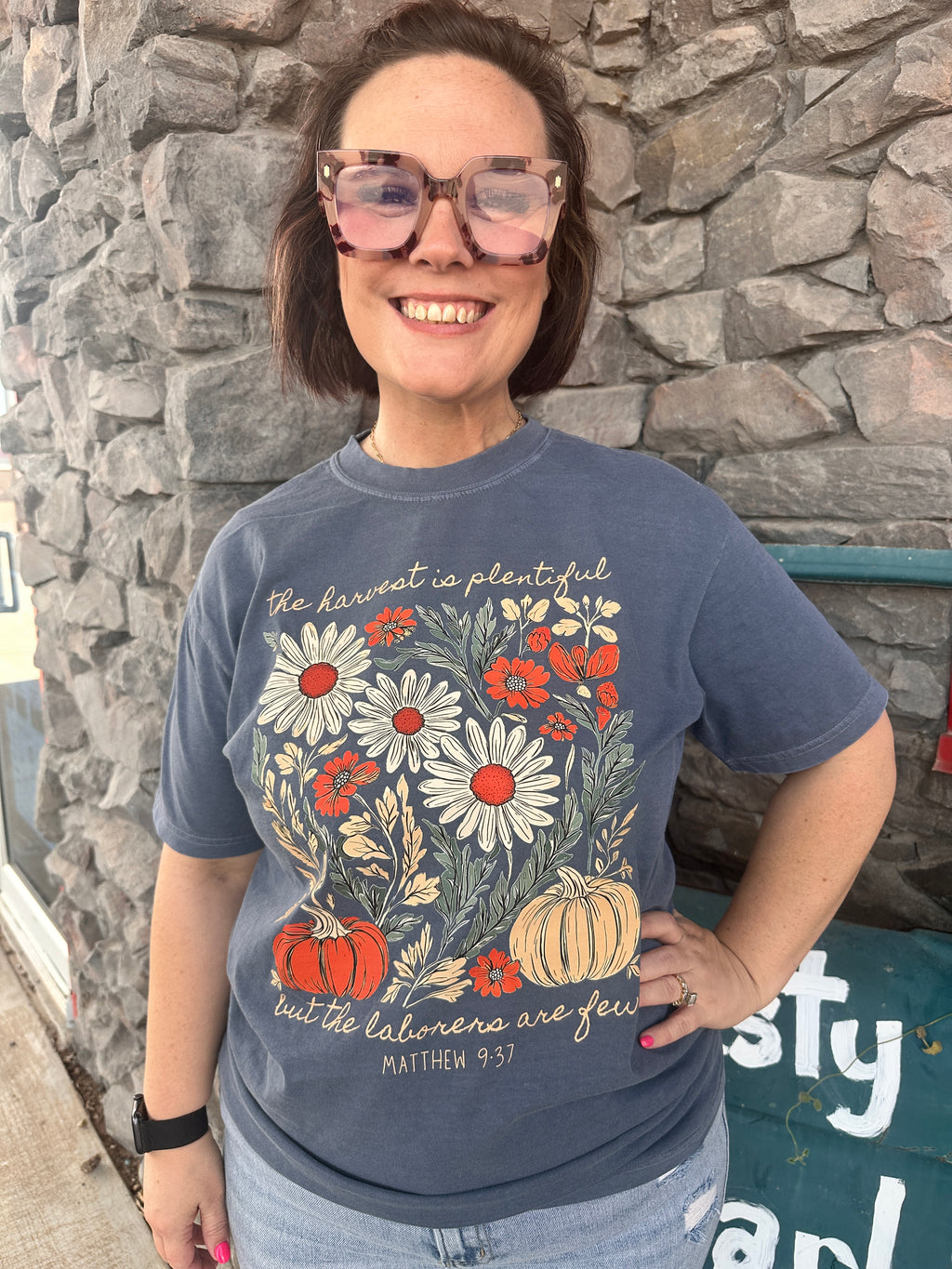 Person wearing a blue t-shirt with floral design and text, standing on a stone surface.