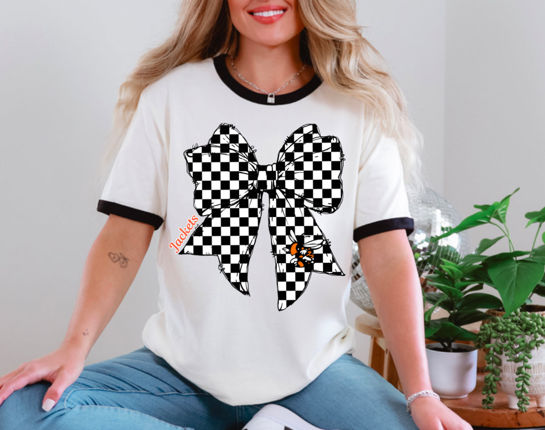 Woman wearing a white t-shirt with a large black and white checkered bow design, sitting indoors.