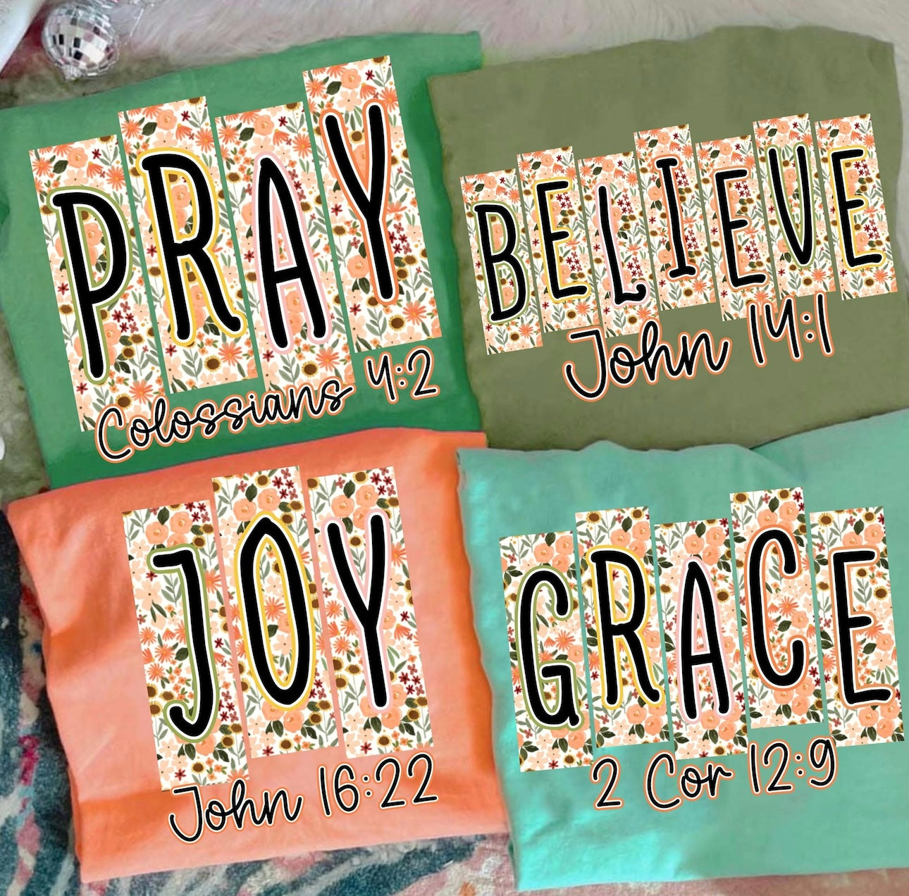 Four T-Shirts with motivational phrases and Bible verses on a textured surface.