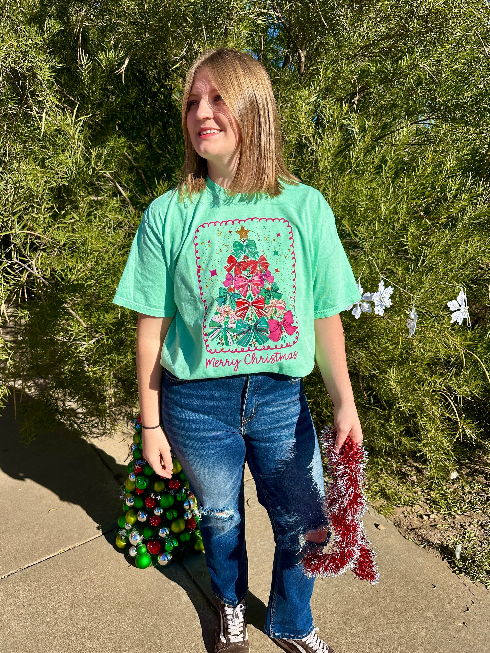 Person wearing a green Christmas-themed t-shirt with decorations outdoors.