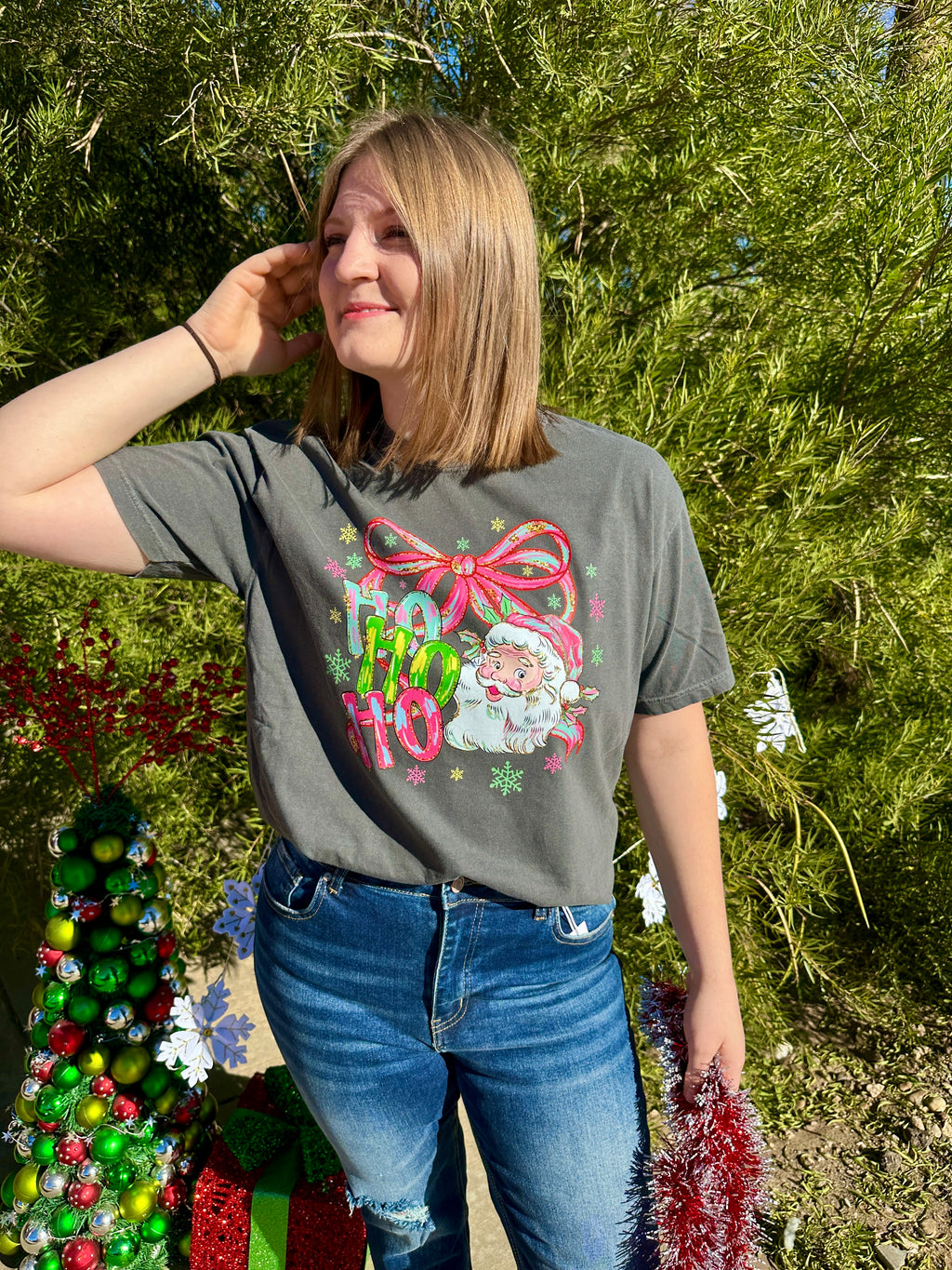 Person wearing a festive t-shirt with a Christmas design in front of a decorated tree.