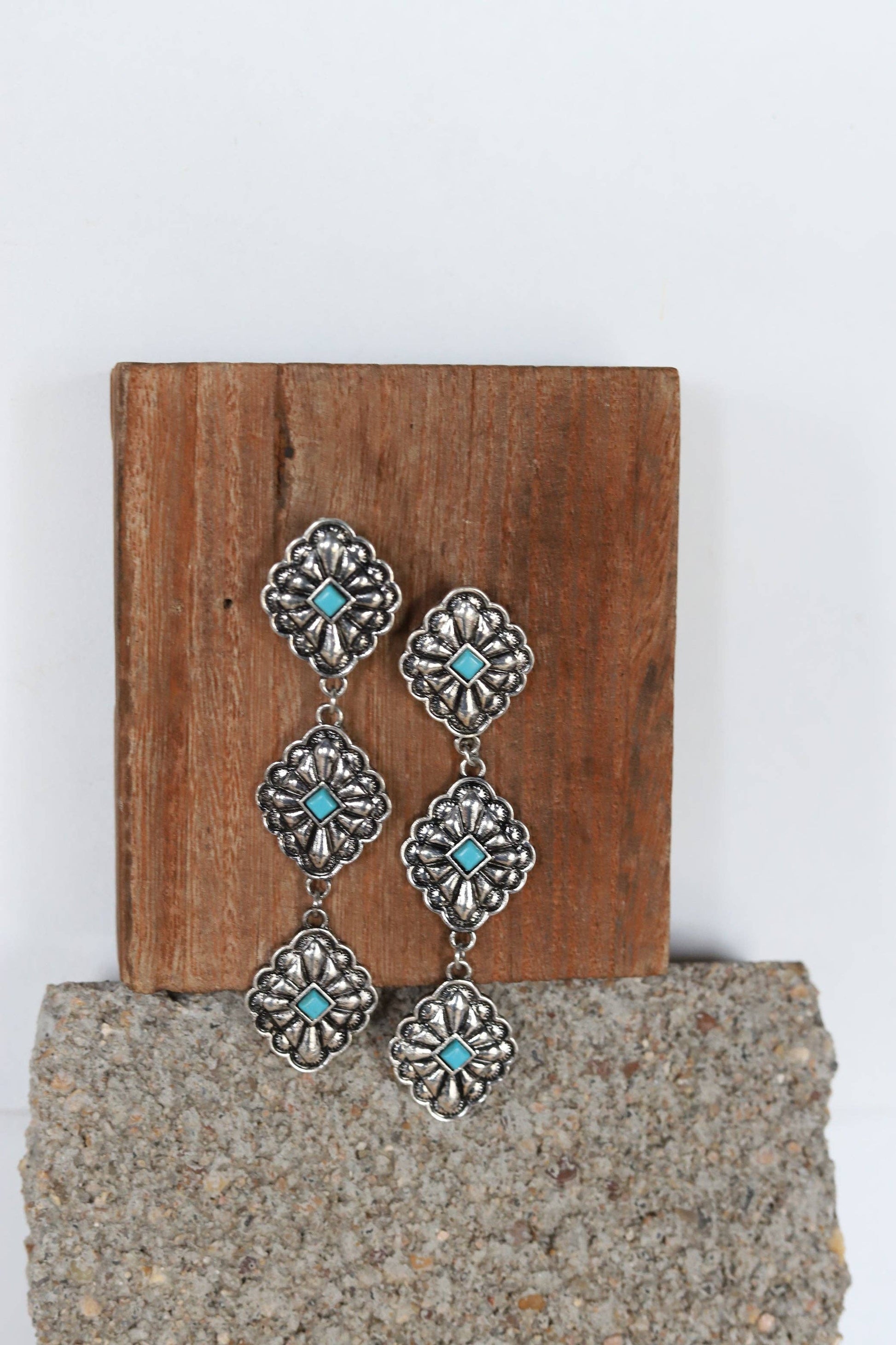 Silver floral earrings with turquoise stones on a wooden block.