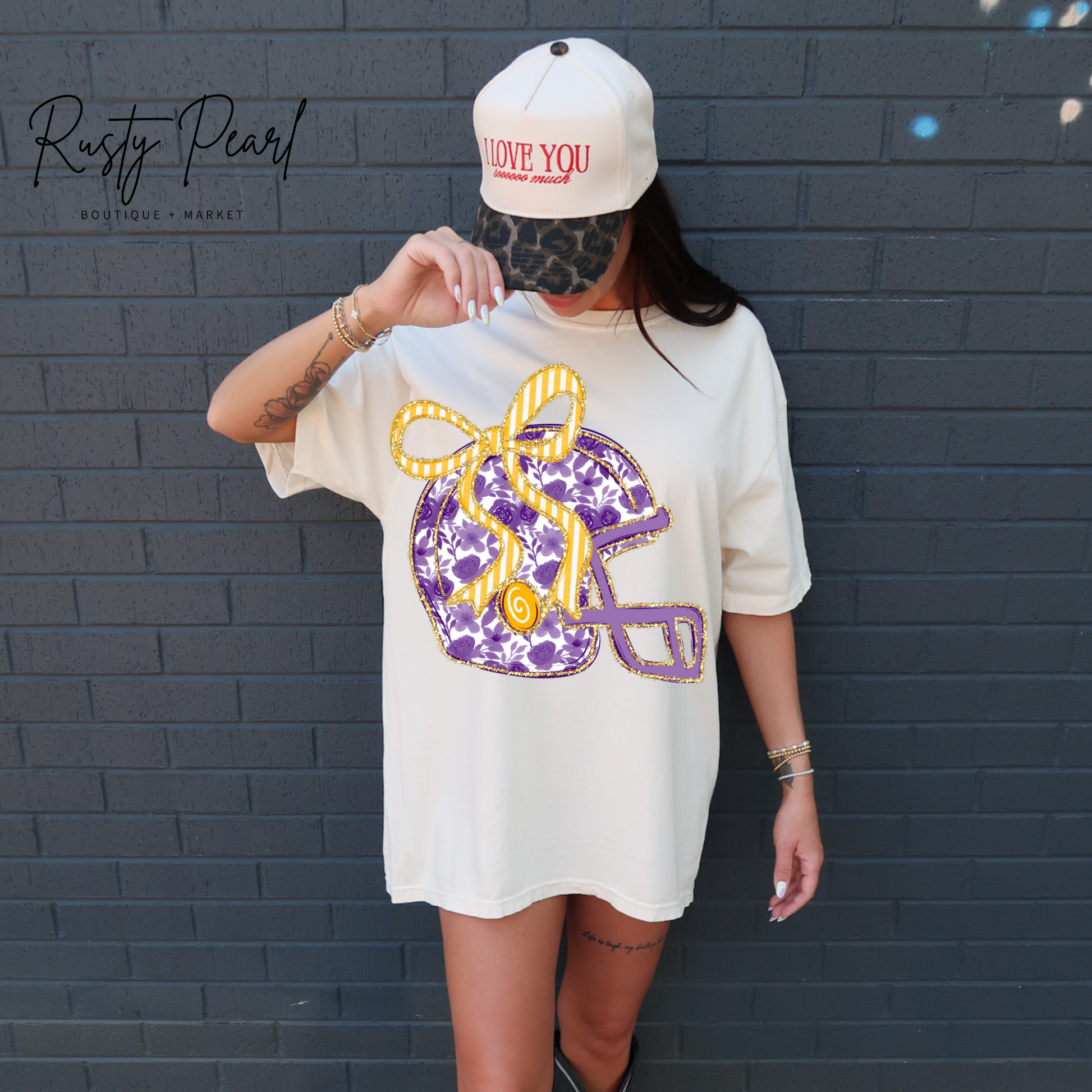 Person wearing a white oversized t-shirt with a colorful graphic design and a cap, standing against a dark brick wall.