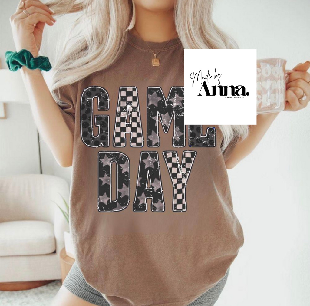 Person wearing a 'Game Day' t-shirt with a checkered design, holding a mug.