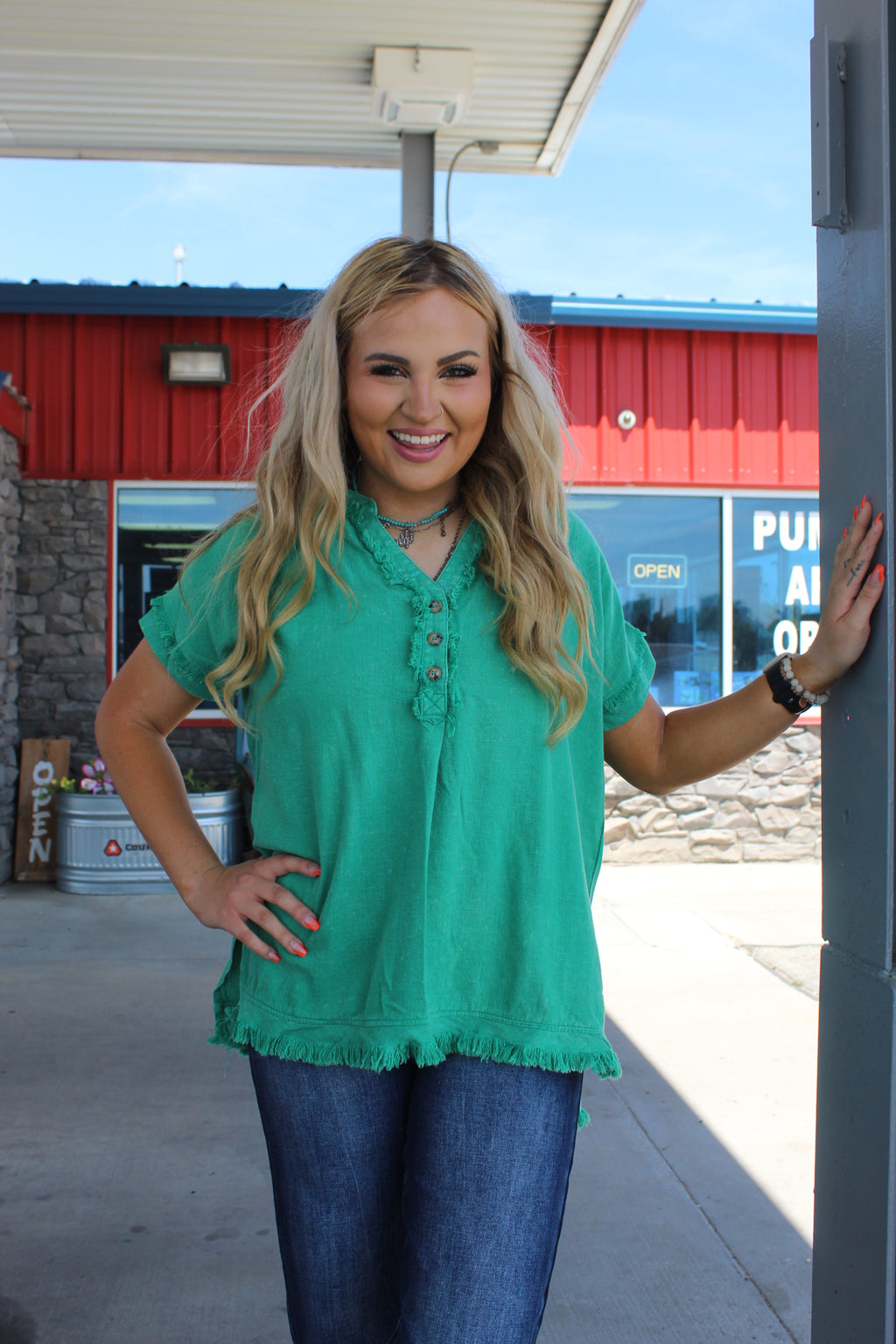 A woman wearing a green blouse with short sleeves and a V-neckline, paired with blue jeans, standing near a red structure.